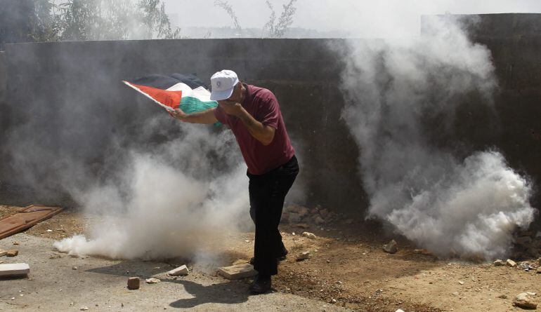 Un palestino se protege de los gases lacrimógenos lanzados por los militares israelíes durante una protesta en contra del asentamiento israelí en Nablús, Cisjordania.