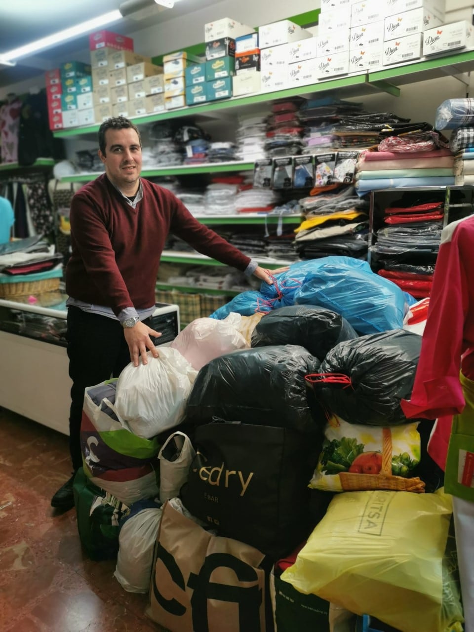 Mikel Izquierdo posa en en interior de su establecimiento con algunas de las bolsas de ropa entregadas