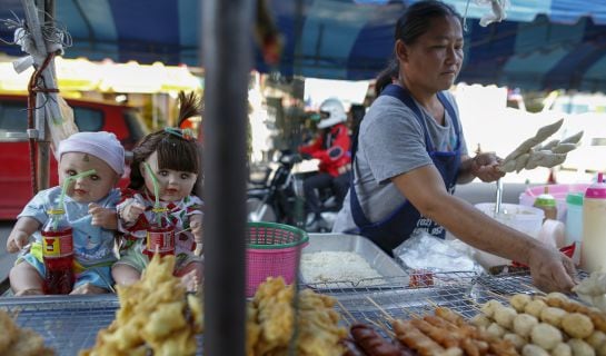 Hong, 42, a street food stall owner, works next to her &quot;child angel&quot; dolls near Wat Bua Khwan temple in Nonthaburi, Thailand, January 26, 2016. A craze for lifelike dolls thought to bring good luck is sweeping Thailand, reflecting widespread anxiety as th