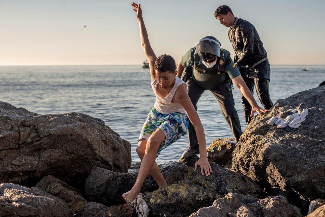 Un menor inmigrante es acompañado por un guardia civil a su llegada este miércoles a nado a la playa ceutí de El Tarajal.