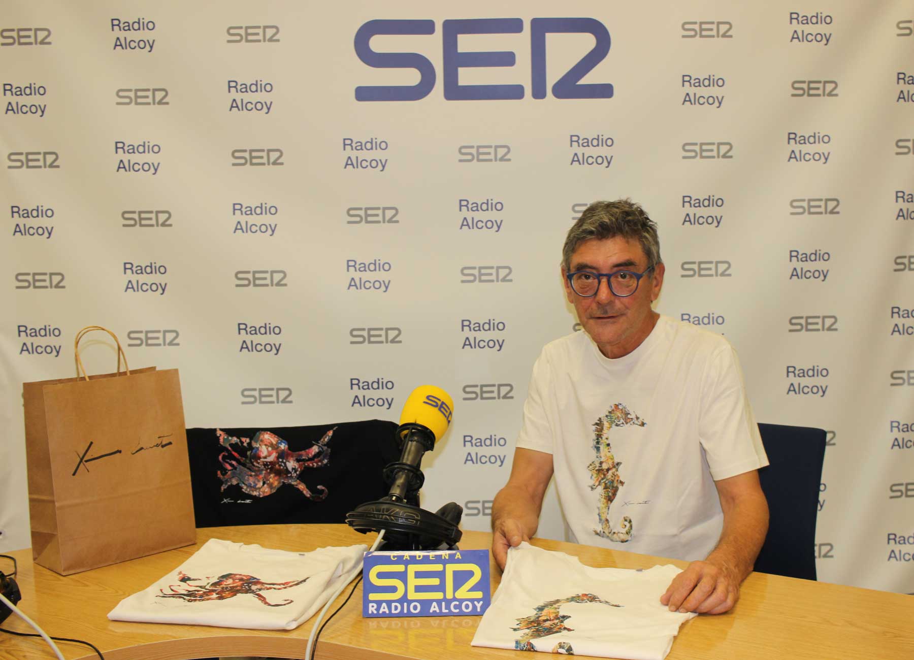 Ximo Canet, en l'estudi central de Radio Alcoy, amb samarretes amb protagonisme de la seua obra