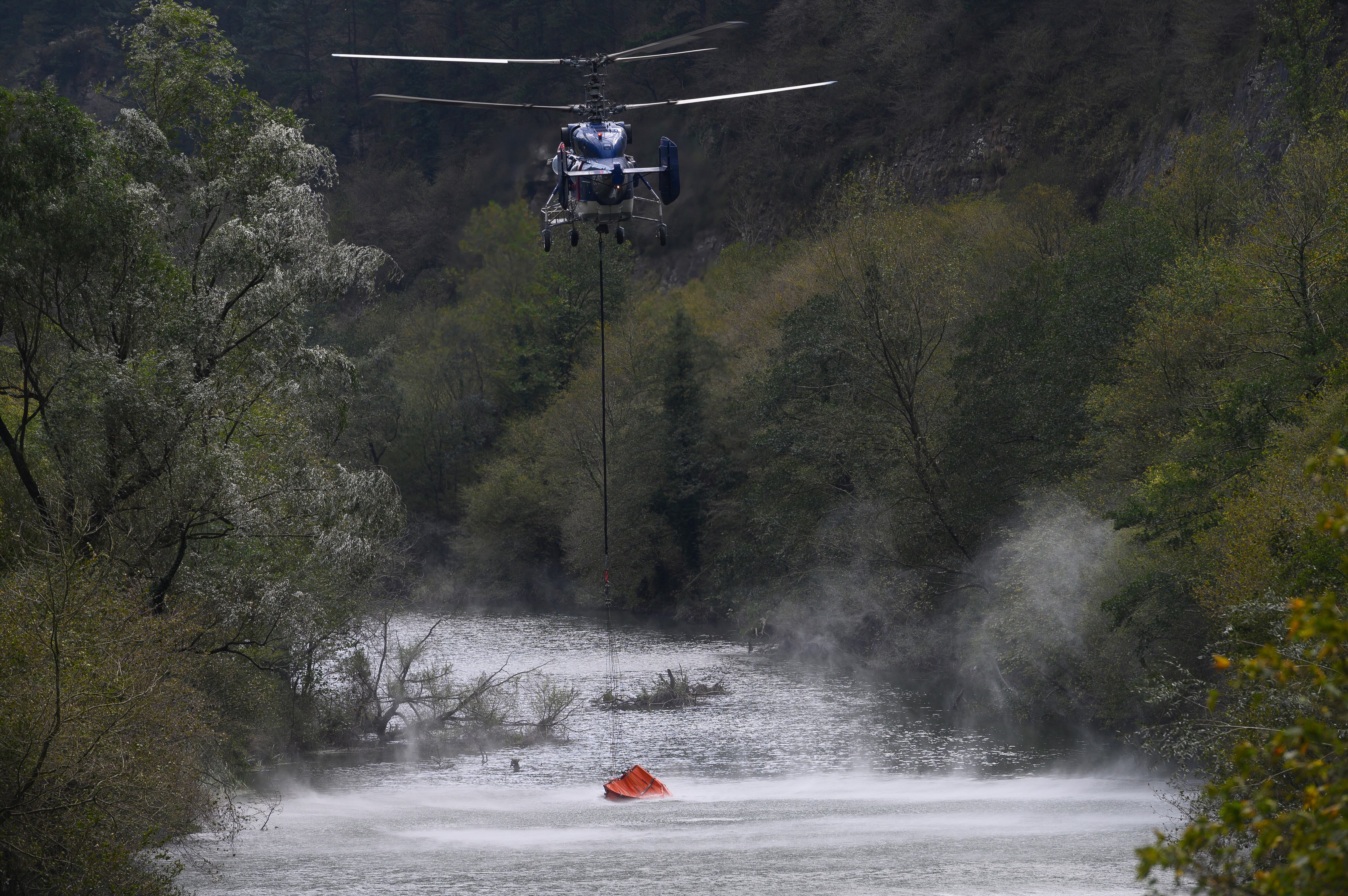 Un helicóptero trabaja en las labores de extinción del incendio forestal declarado este sábado en la localidad cántabra de Bostronizo. EFE/Pedro Puente Hoyos