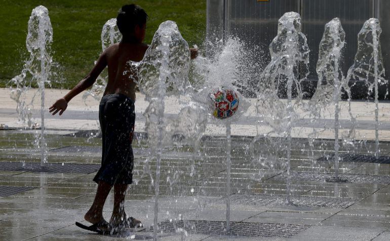 GRA323 MADRID, 06/07/2015.- Un niño juega con la pelota intentando aliviar el calor en una de las fuentes del parque Juan Carlos I en Madrid, en la segunda ola de calor que alcalzará hoy su pico con máximas de hasta 45 grados.- EFE/JUANJO MARTIN