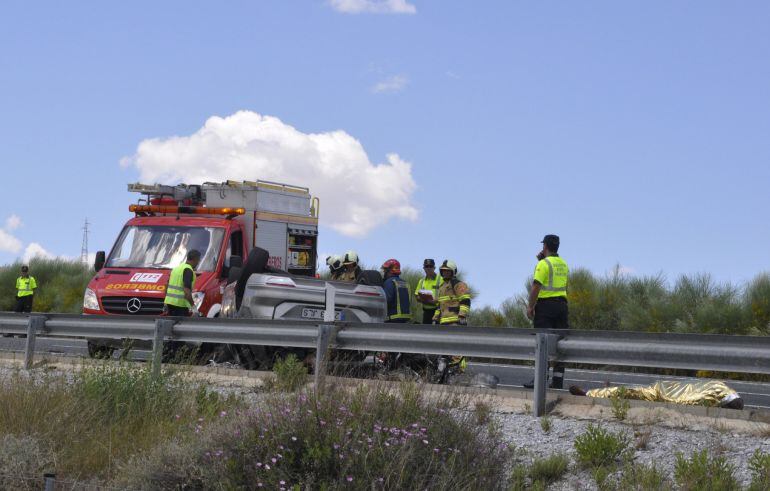 Bomberos y Guardia Civil junto a un vehículo volcado y el cuerpo de uno de los tres fallecidos en el accidente de tráfico ocurrido este mediodía en la autovía A-92N Norte que ha permanecido cortada a la altura del kilómetro 39 en el término municipal de B