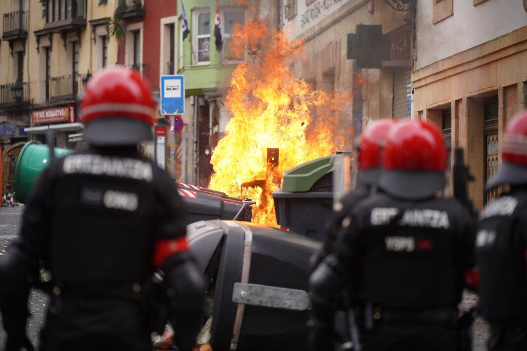 Varios agentes de la Ertzaintza observan como se quema un contenedor durante los altercados producidos en una manifestación contra el encarcelamiento de Pablo Hasel en el sexto día de protestas, en la Plaza de Arriaga, Bilbao,