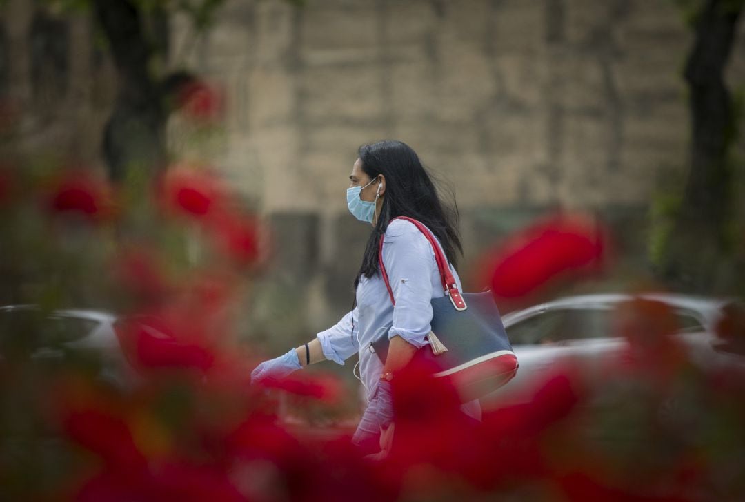 Una mujer andando por Sevilla con mascarilla y guantes 