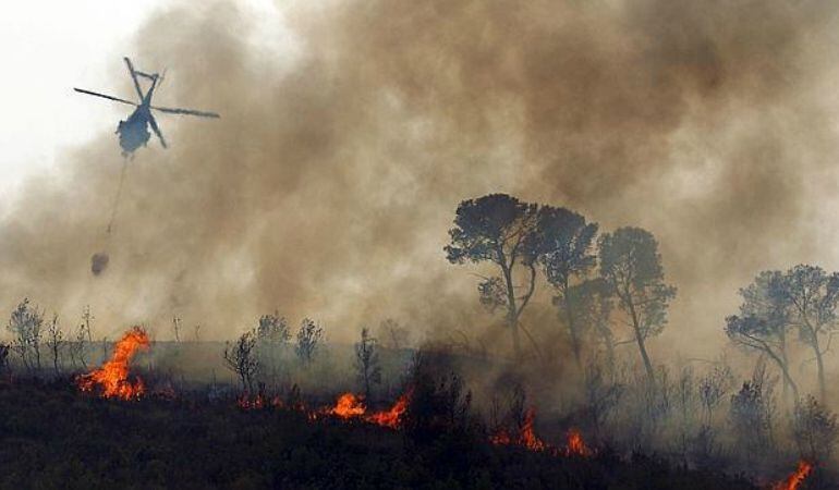 Un helicóptero rocía de agua una zona en llamas. 