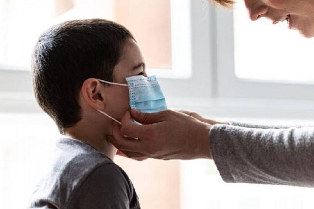 Una madre coloca la mascarilla a su hijo
