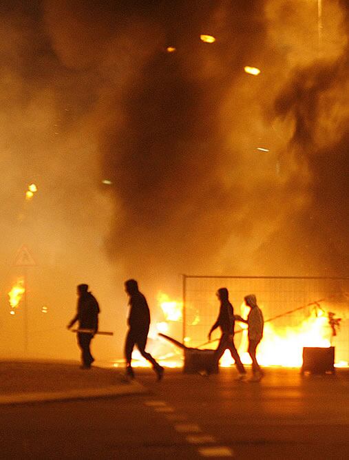 Jovenes de la periferia de París frente a barricadas incendiadas.