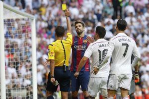 El árbitro Gil Manzano saca la tarjeta amarilla al defensa del FC Barcelona Gerard Piqué ante los jugadores del Real Madrid, James Rodríguez y Cristiano Ronaldo durante el partido de la novena jornada de Liga de Primera División disputado esta tarde en el