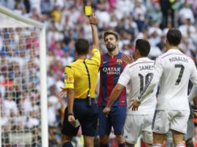El árbitro Gil Manzano saca la tarjeta amarilla al defensa del FC Barcelona Gerard Piqué ante los jugadores del Real Madrid, James Rodríguez y Cristiano Ronaldo durante el partido de la novena jornada de Liga de Primera División disputado esta tarde en el