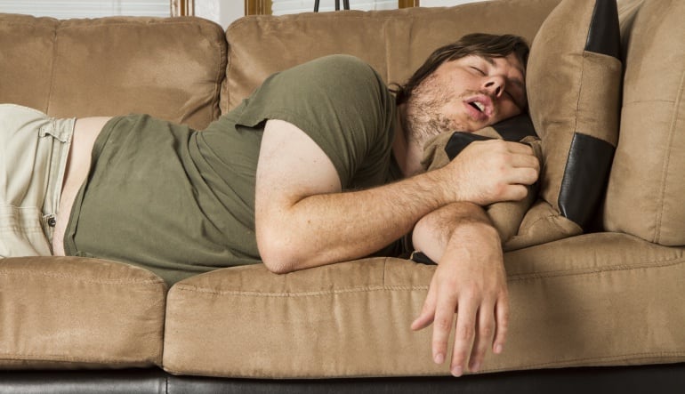 Imagen de un chico durmiendo la siesta a pierna suelta en un sofá. 