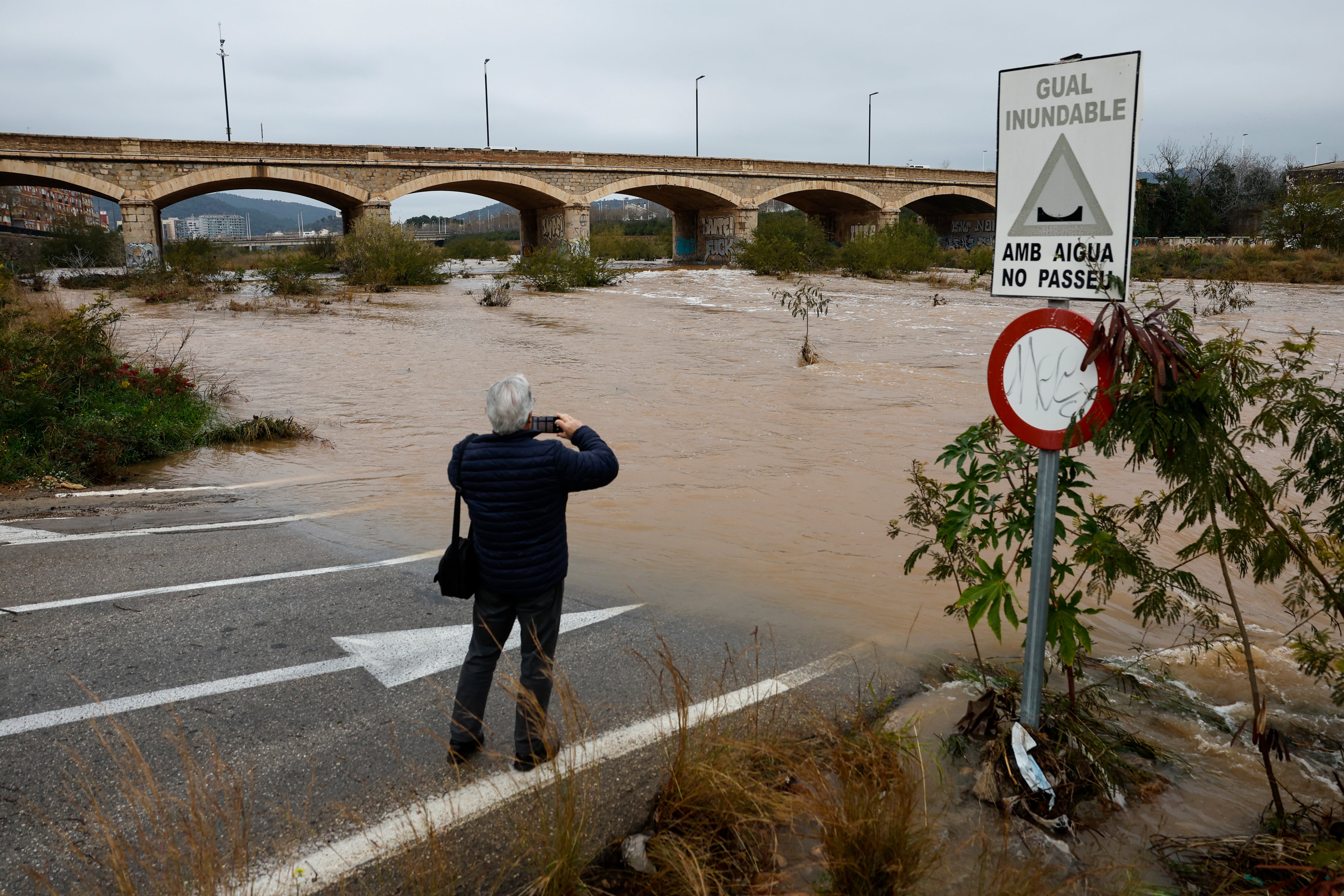 Una persona toma una imagen del caudal del río Palancia a su paso por Sagunto cuando varias carreteras de las provincias de Valencia y Castellón permanecen cortadas debido a la lluvia.