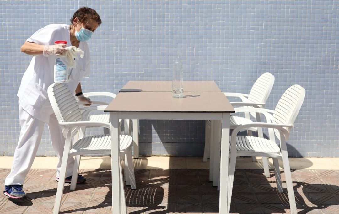 Una mujer desfinfecta la mesa de una terraza de un bar.