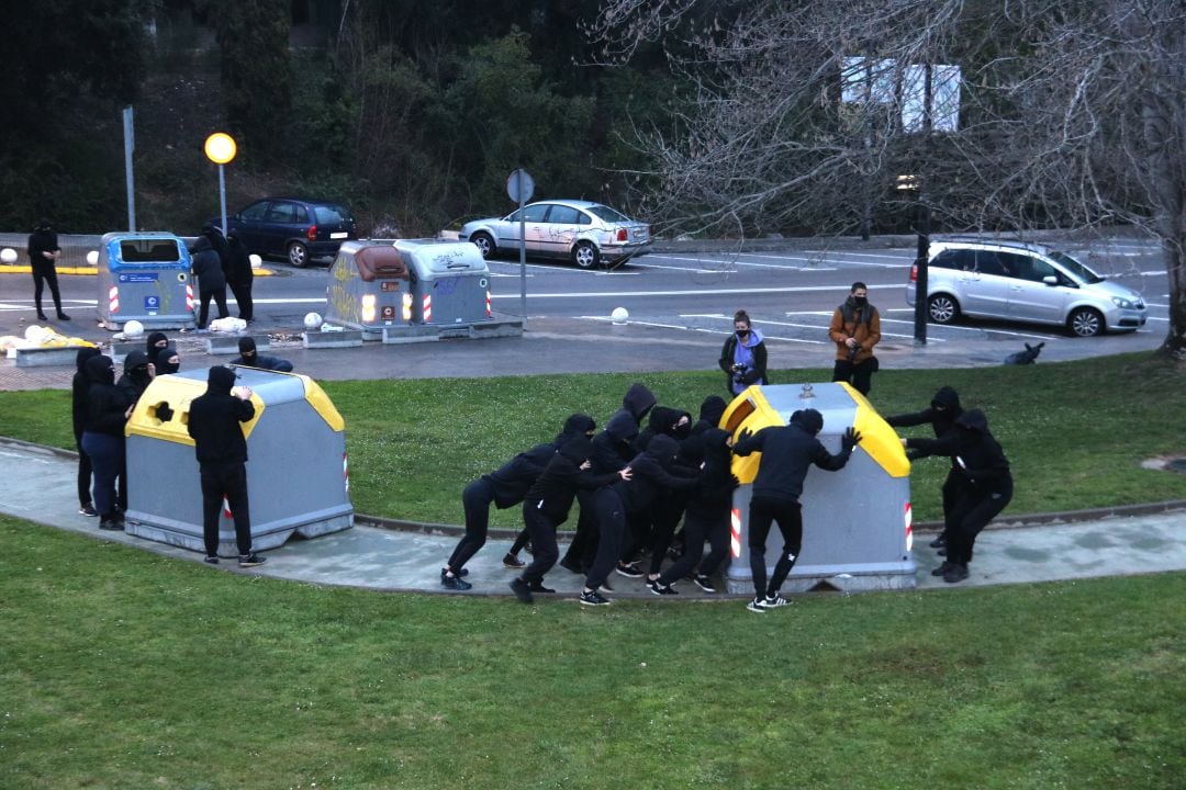 Un grupo de pesonas empujan contenedores en el acceso al campus Bellaterra de la UAB