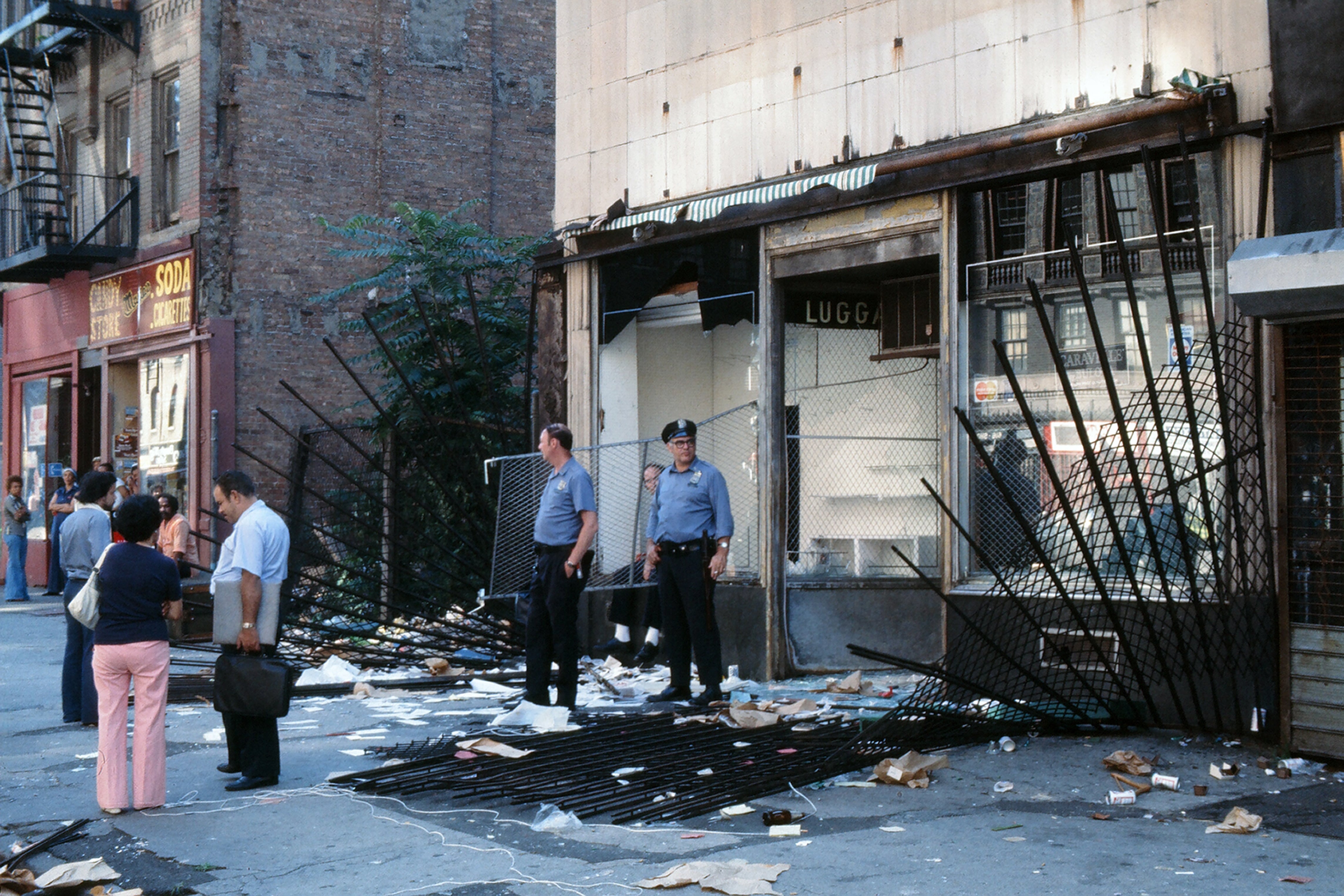 Policías y transeúntes frente a la fachada de una tienda dañada, saqueada tras el apagón de Nueva York, Brooklyn, Nueva York, 14 de julio de 1977. (Foto de Robert R. McElroy/Getty Images)