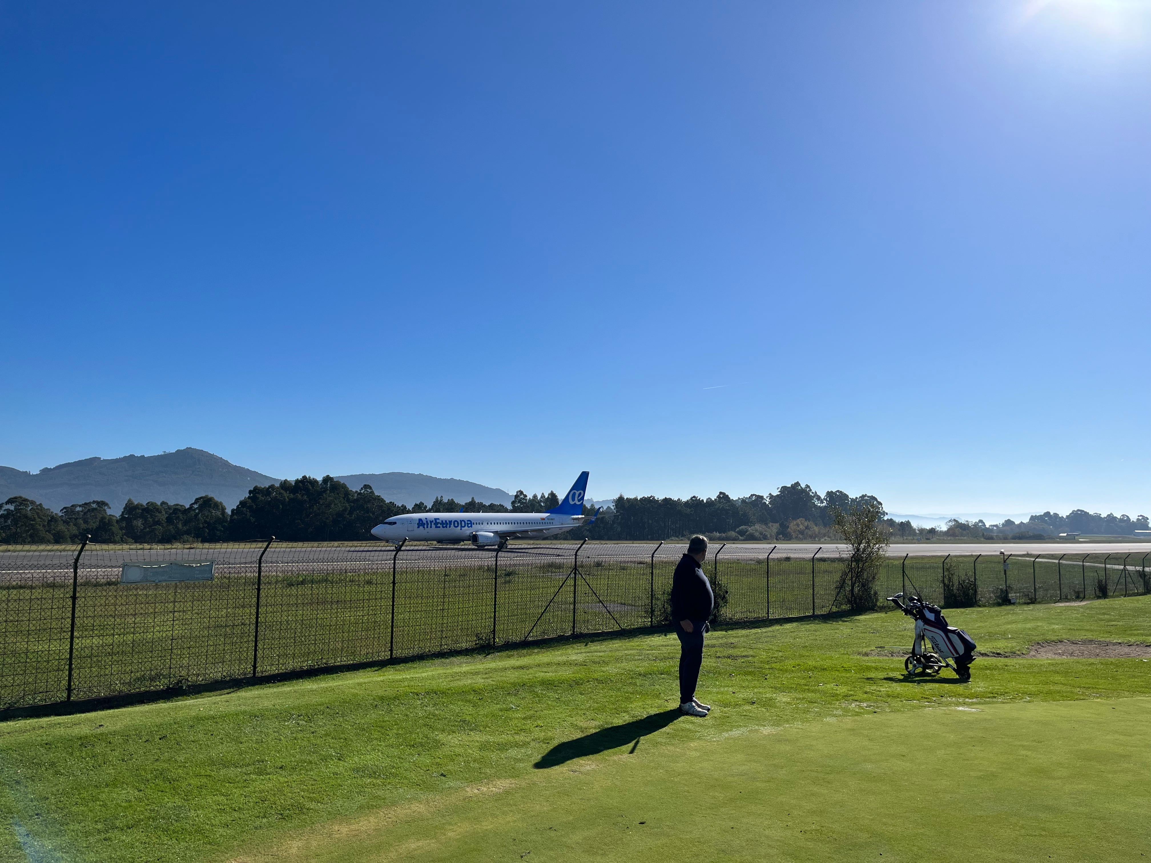 Un avión aterriza en Peinador junto a un jugador del Aeroclub, en uno de los hoyos del campo de golf que desaparecerán con la expropiación de AENA