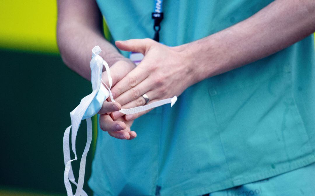 Un sanitario aplaude con la mascarilla entre las manos.