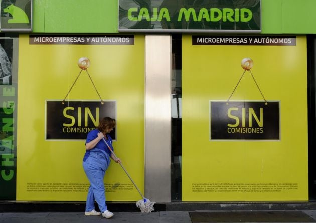 Una mujer limpia la entrada de una oficina de Bankia en Sevilla