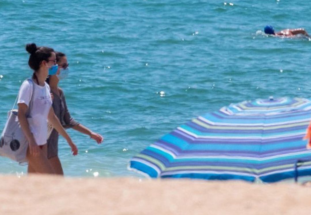 Dos mujeres pasean por la playa llevando mascarilla