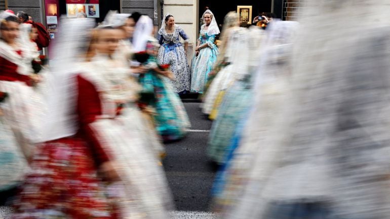 Dos falleras contemplan el paso de sus compañeras en el primer día de la ofrenda a la Virgen de los Desamparados, el acto más multitudinario de las fallas de Valencia en el que falleras y falleros depositan flores con las que se forma el manto de la patro