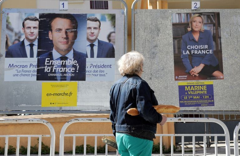 Una mujer camina cerca de la propaganda electoral de Macron y Le Pen. 