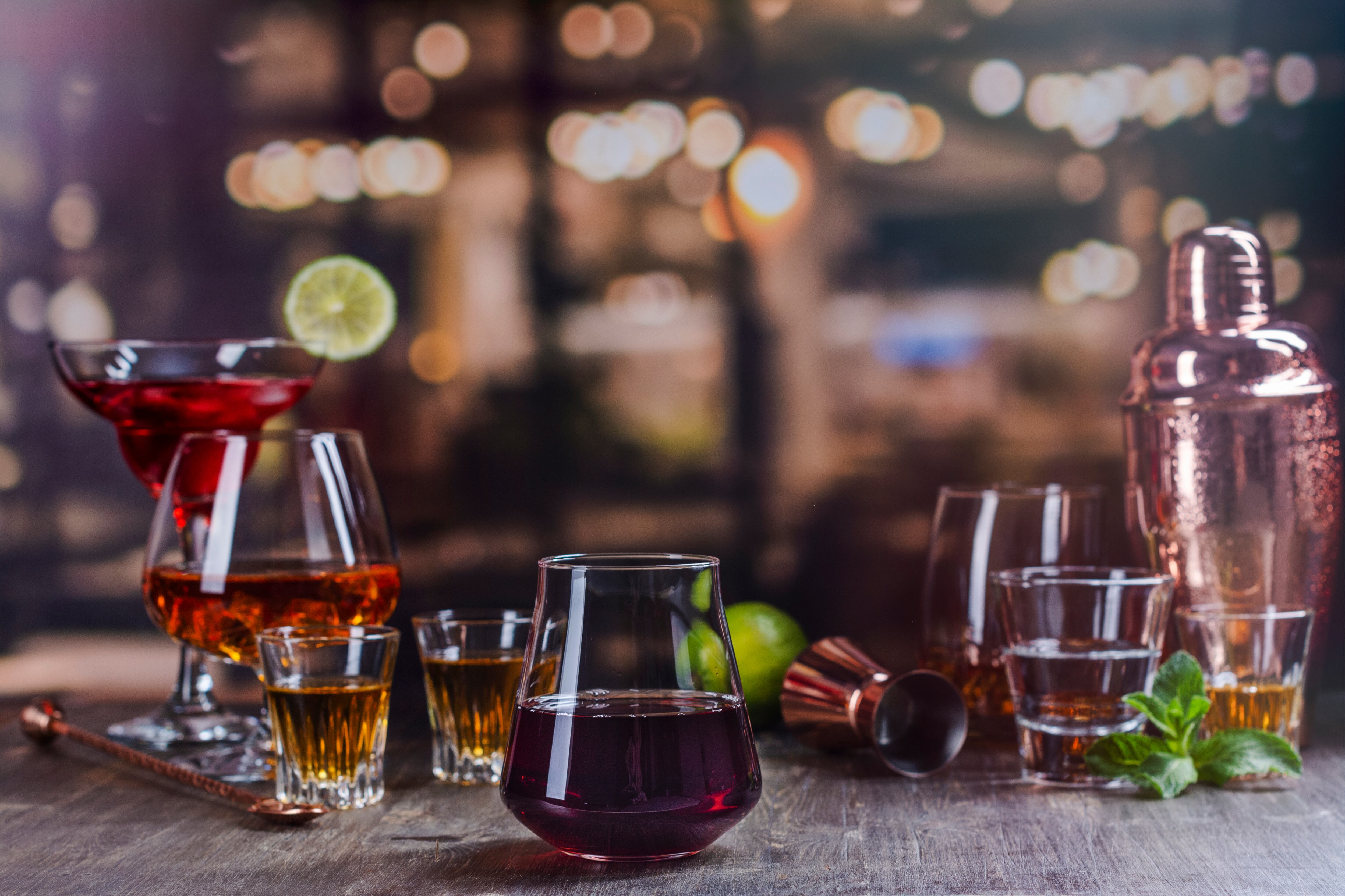 Red wine in a glass on a bar counter. Assortment of different strong alcohol drinks over night lights background. Copy space