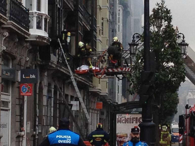 Los bomberos evacúan el cuerpo de su compañero fallecido por la ventana del edificio incendiado