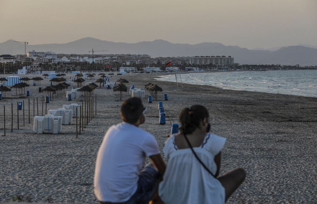 Dos jóvenes sentados contemplan la playa de la Malvarrosa durante la noche de San Juan del año pasado.