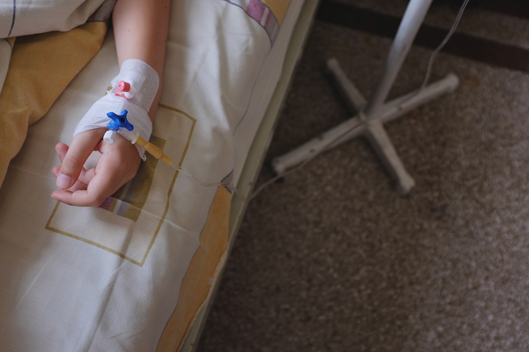 Mano de un paciente, con la vía puesta, en una cama de hospital