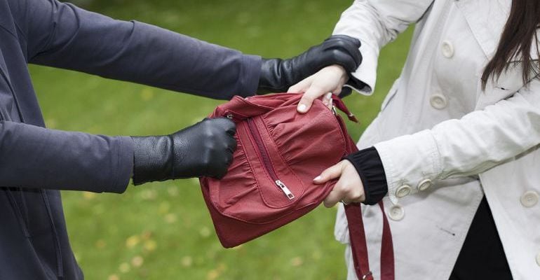 Una persona intenta quitar el bolso a una mujer por el procedimiento del tirón.