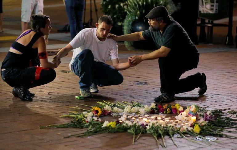 Dos personas rinden homenajes a uno de los fallecidos.