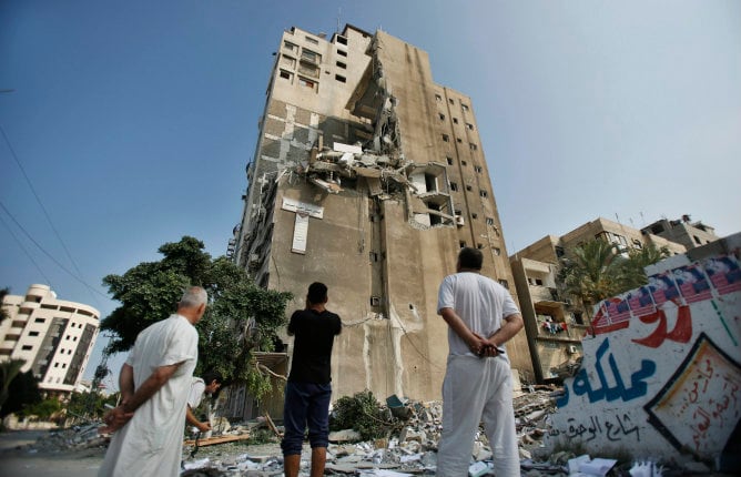 Varias personas observan un edificio residencial que fue golpeado en un ataque aéreo israelí que mató al menos a 10 palestinos el lunes