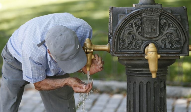 Un hombre bebe en una fuente del parque del Retiro, en Madrid.