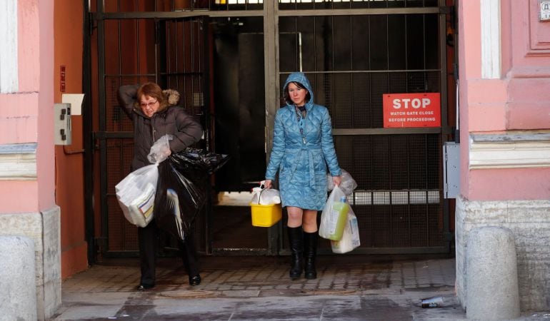 Dos mujeres cargan con varias bolsas mientras salen del Consulado General de EE. UU. en San Petersburgo (Rusia).