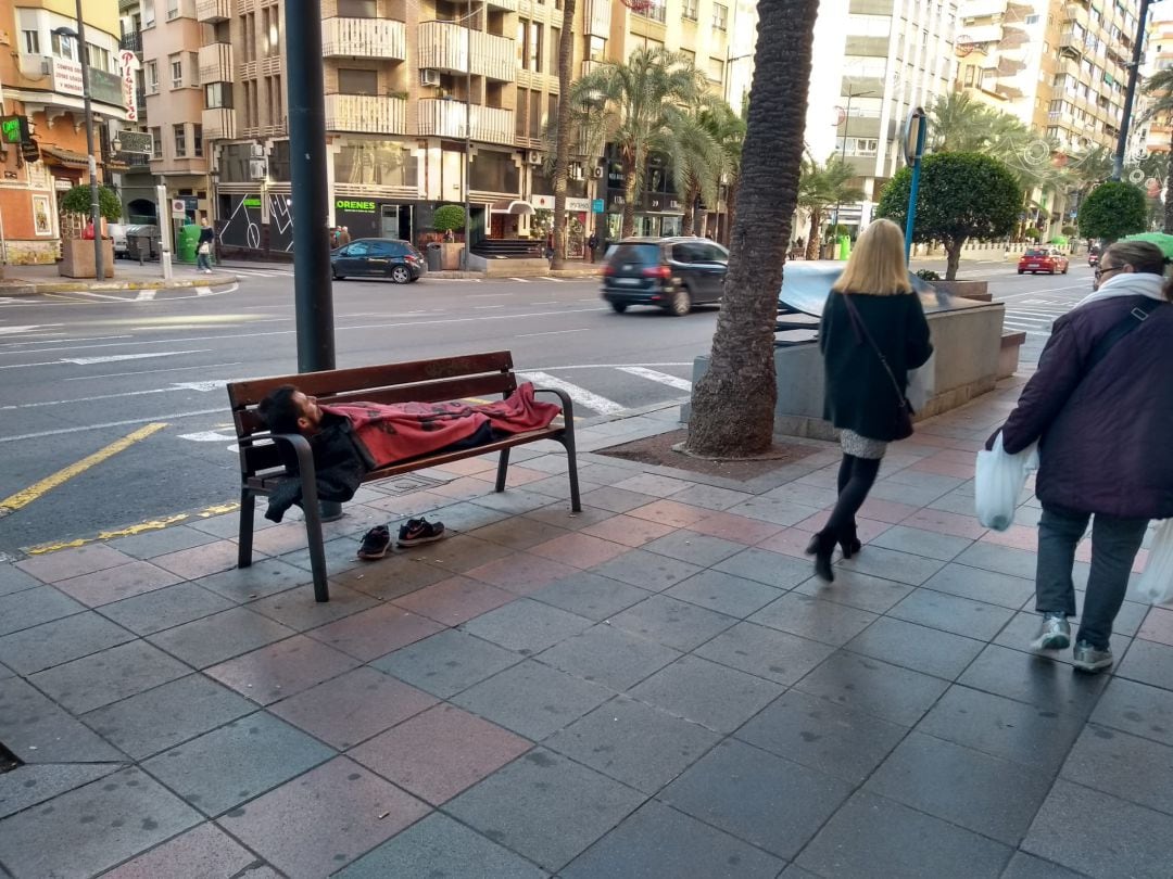 Una persona duerme en un banco en la avenida Alfonso el Sabio, de Alicante.