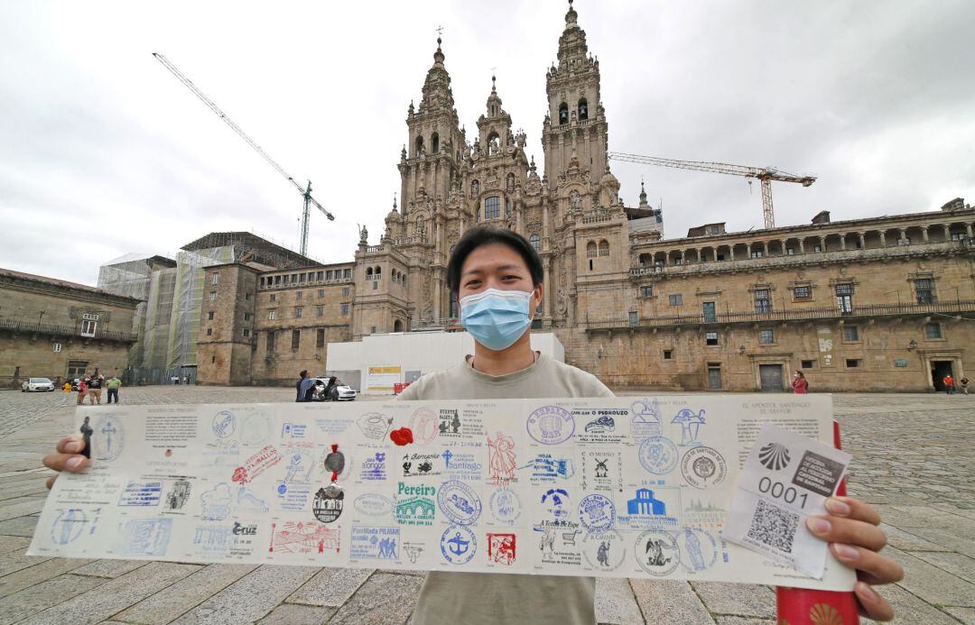 El primer peregrino en haber completado el camino tras su reapertura, el chino Liam Duam, muestra la "Compostela", o certificado de haber completado la ruta en la plaza del Obradoiro este miércoles en Santiago de Compostela.