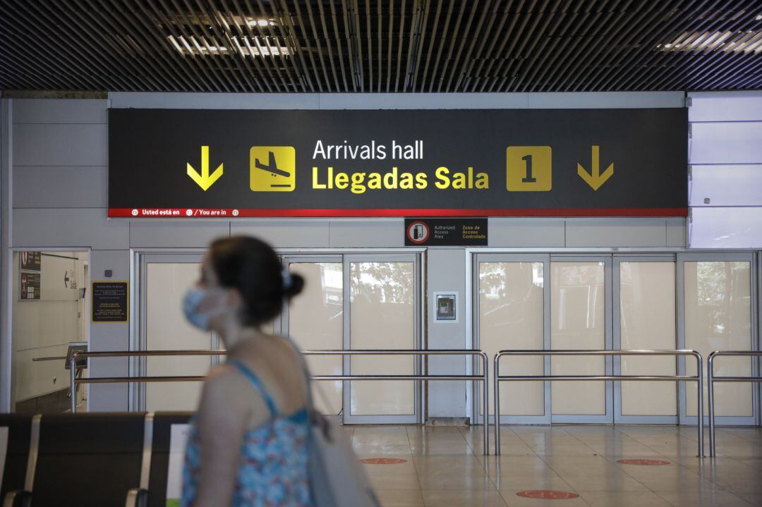 Una persona con mascarilla pasa junto a la entrada de la sala de llegadas  en un aeropuerto
