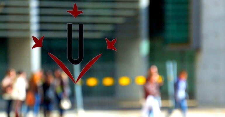 Imatge d'estudiants reflectits en una porta de vidre amb el logotip de la Universitat de Lleida.