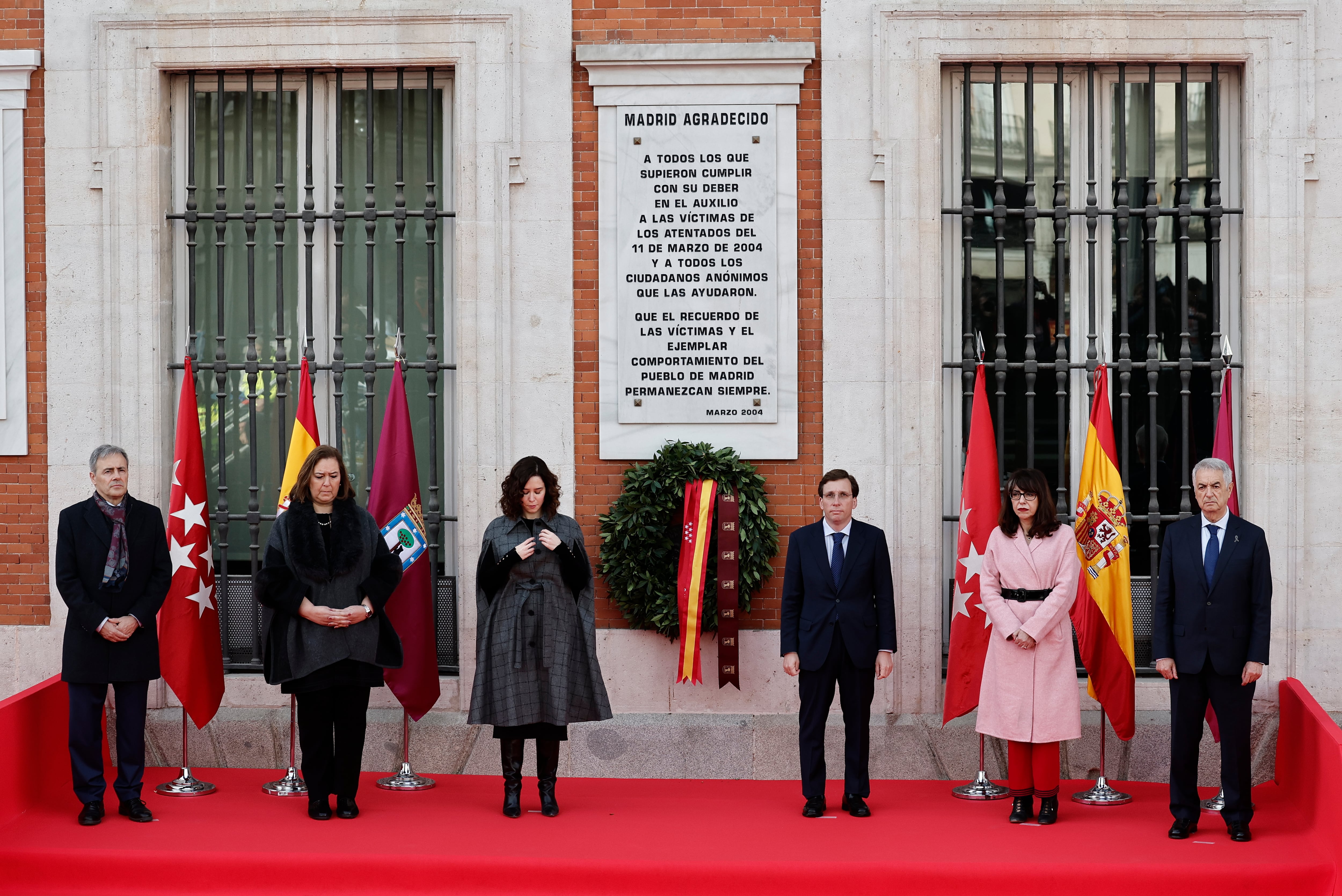 La presidenta de la Comunidad de Madrid, Isabel Díaz Ayuso (c-i), y el alcalde de la capital, José Luis Martínez-Almeida (c-d), acompañados por (de izq a der) el presidente de la Fundación Víctimas del Terrorismo, Tomás Caballero; la presidenta de la Asociación Víctimas del Terrorismo, Maite Araluce; la presidenta de la Asociación de Ayuda a las Víctimas del 11-M, Dori Majali, y el presidente de la Asociación 11M Afectados del Terrorismo, Eulogio Paz, permanecen junto a la corona colocada bajo la placa que homenajea a las víctimas del atentado del 11-M, este sábado, aniversario de la tragedia, ante la Real Casa de Correos, sede del gobierno regional. EFE/ Sergio Pérez