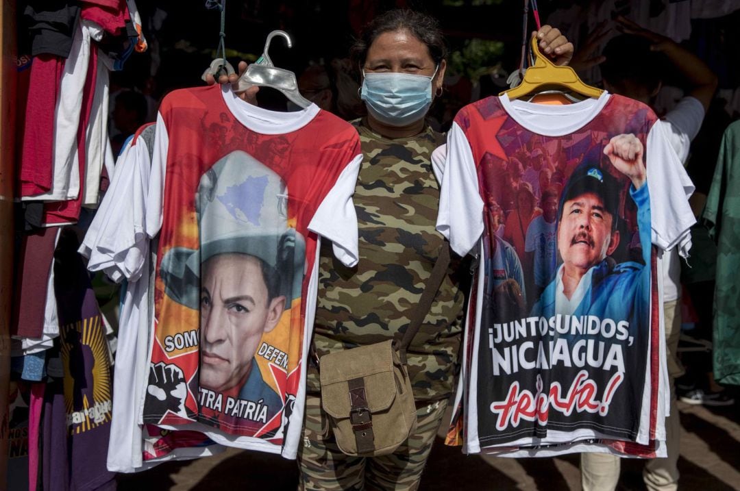 Una mujer posa para una fotografiá sosteniendo dos camisetas que muestran la imagen del héroe nacional Augusto C. Sandino (i) y el presidente de Nicaragua Daniel Ortega (d), en Managua (Nicaragua). El izquierdista Frente Sandinista de Liberación Nacional (FSLN) de Nicaragua ha celebrado su 60 aniversario con absoluto, aplastando a sus rivales internos, gobernando mediante la represión y el miedo, aislado y enfrentado con Occidente, y con el apoyo de Rusia, Cuba, Venezuela, Irán y Taiwán.