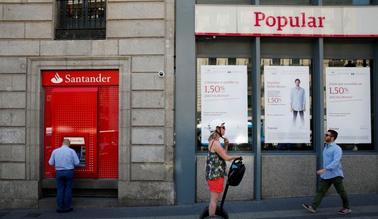 A man uses a cash dispenser at a branch of Spain&#039;s biggest bank Santander next to a Banco Popular branch in Madrid