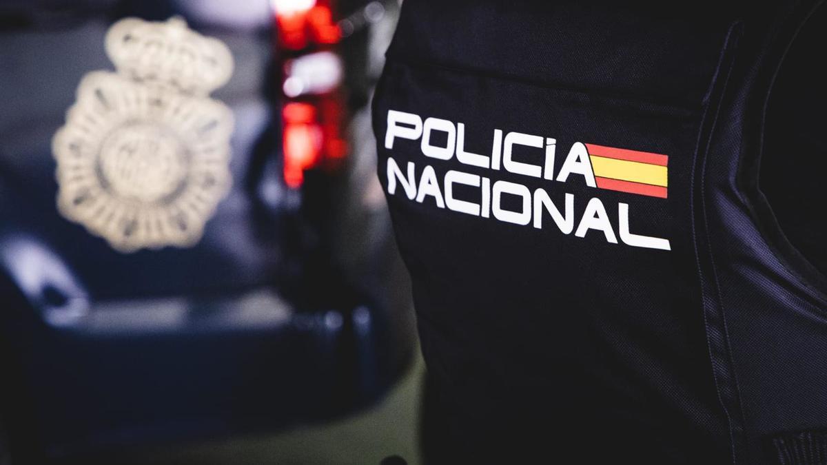 Imagen de un agente de la Policía Nacional frente a un coche logotipado del cuerpo.