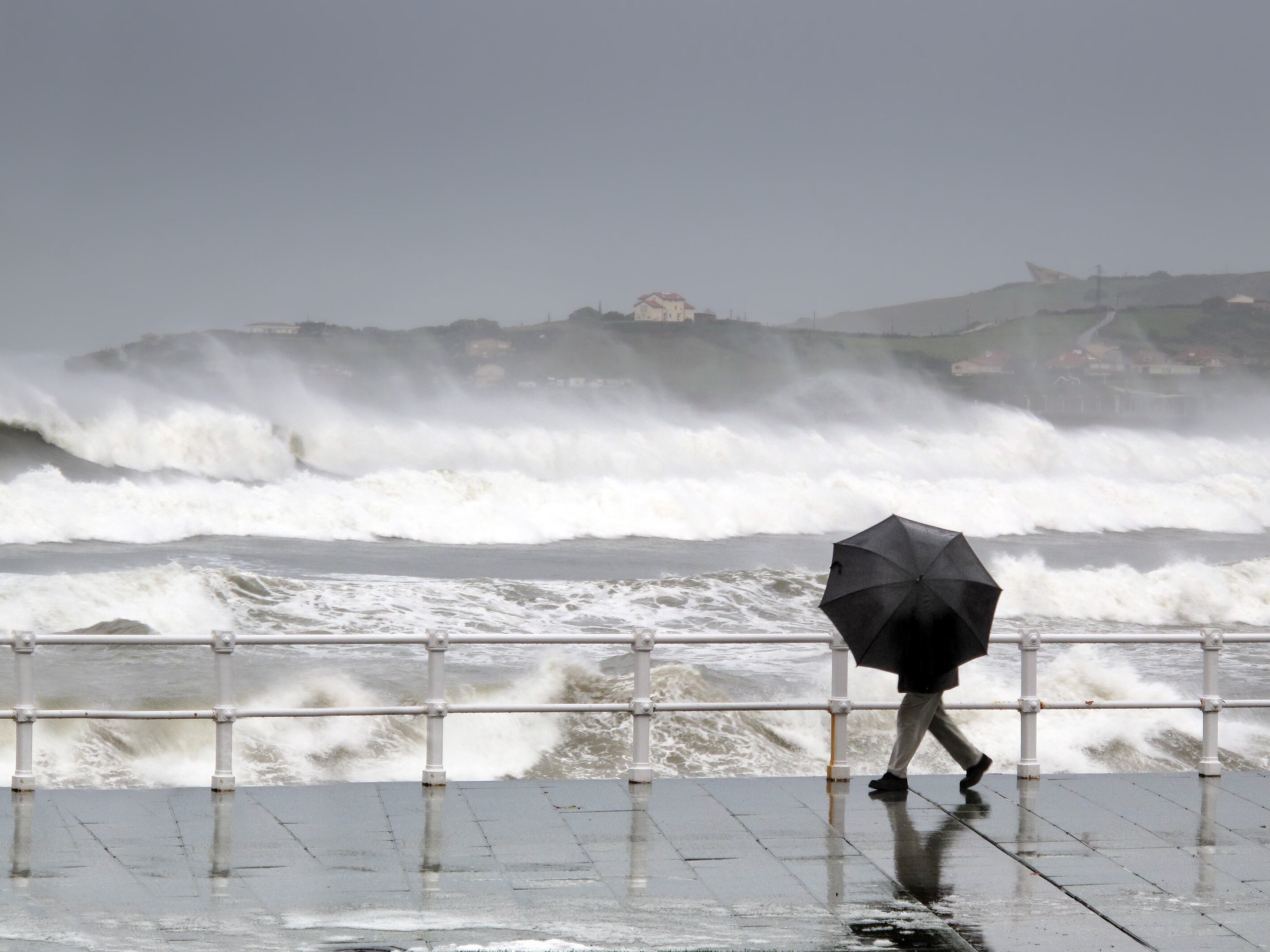 Una persona se protege de la lluvia durante su paseo junto al mar.