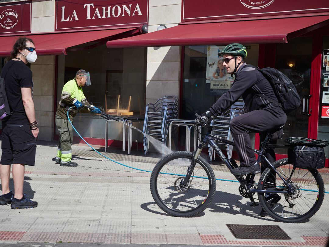 Un hombre pasa en bicicleta mientras un trabajador aparece en labores de limpieza y desinfección de una panadería durante el día 54 del estado de alarma en Pamplona 