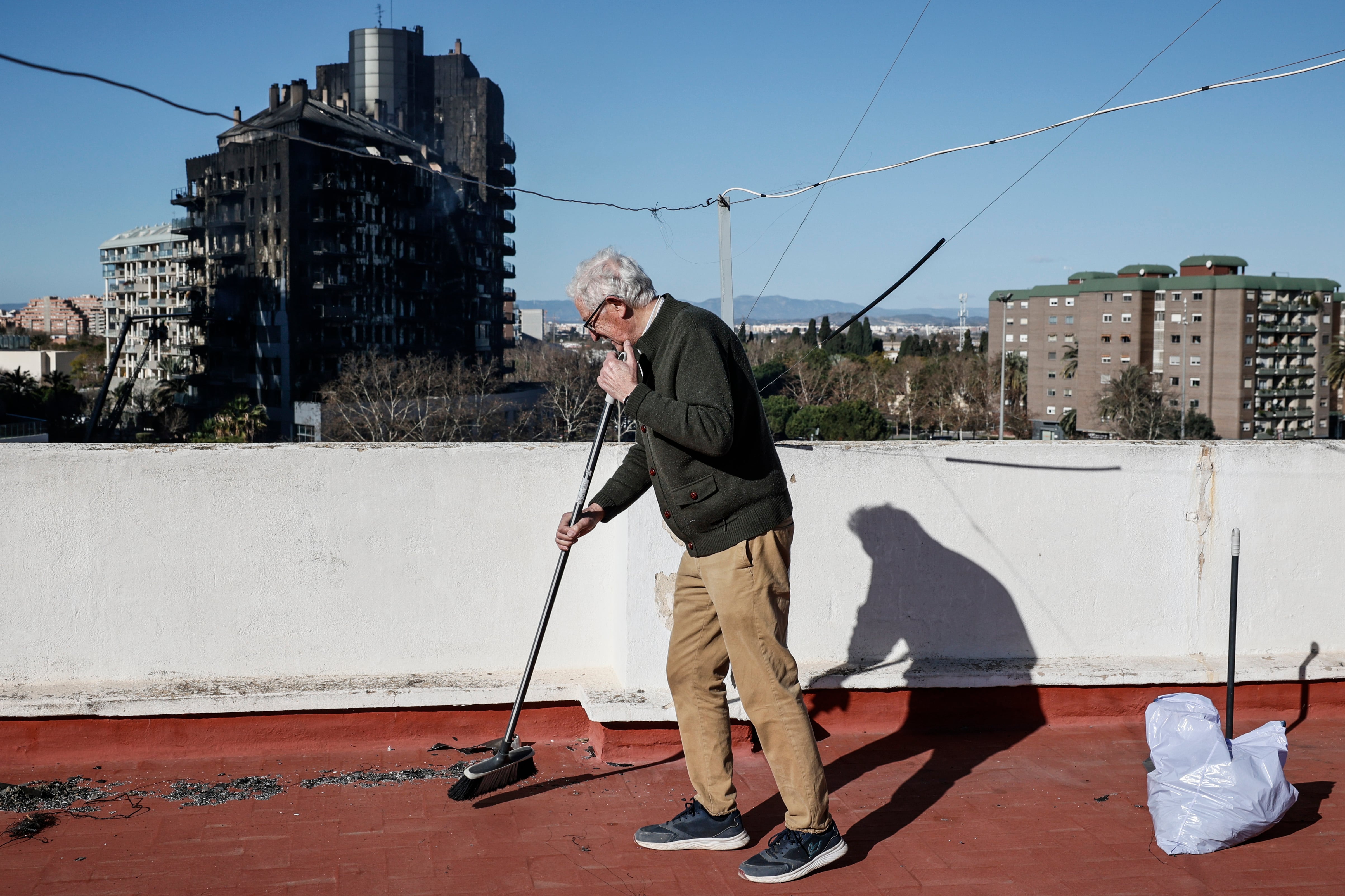 Un vecino barre las cenizas que se han acumulado en la terraza de su vivienda frente a los edificios incendiados.