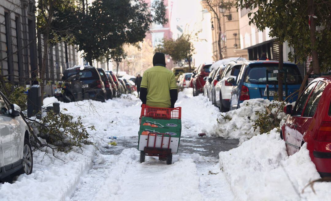 Un hombre arrastra una carretilla por una calle del centro aún con nieve y árboles caídos en Madrid (España).