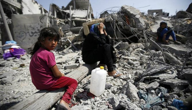 Hala Al Kafarna, de 6 años, sentado junto a varios familiares entre los escombros de su casa en la localidad de Beit Hanun (Gaza)