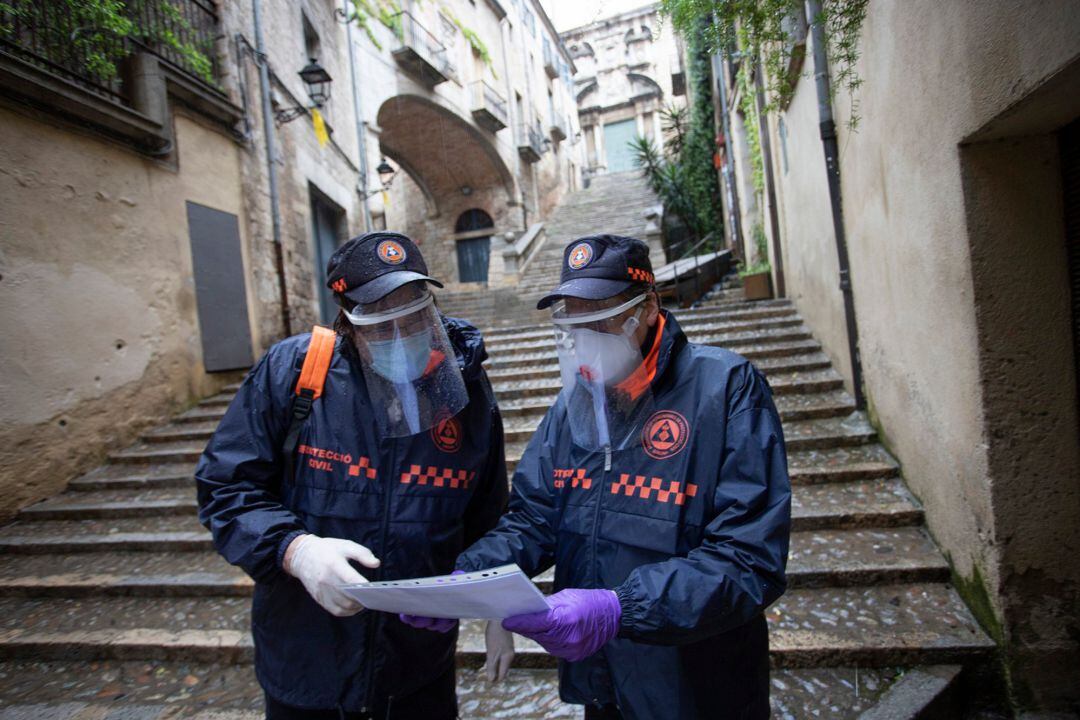 Pla general de dos voluntaris de Protecció Civil de Girona consultant un llistat per saber a quines cases han d'entregar mascaretes per a persones grans