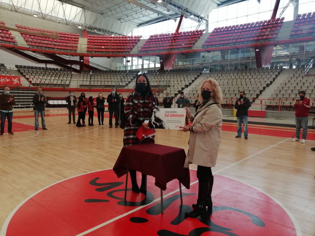 La mujer y una de las hijas de Ed Johnson muestran la placa de homenaje que se ubicará en una de las columnas del Palacio de Deportes de La Guía.